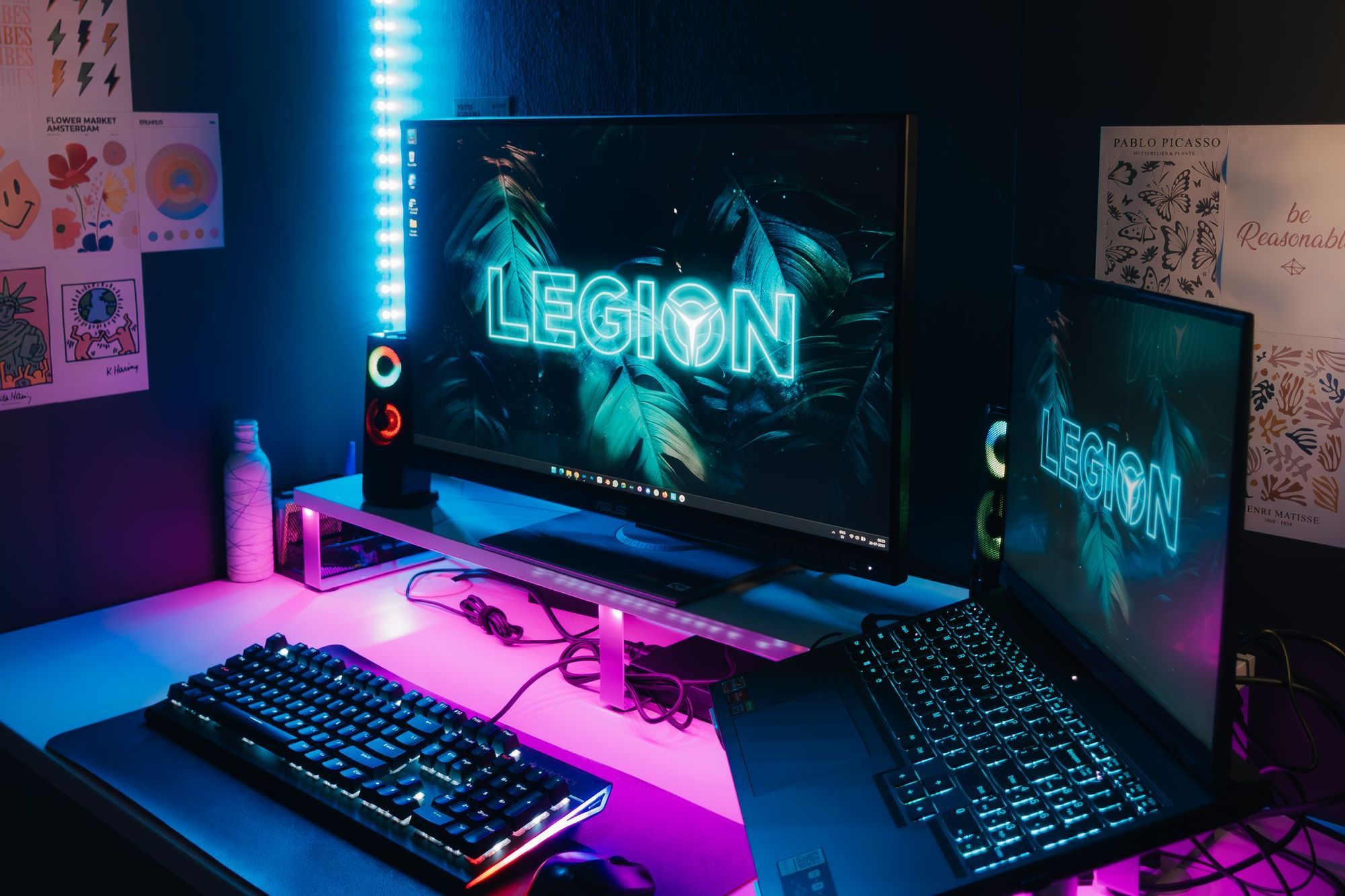 A desk setup with monitors and RGB keyboards in neon light