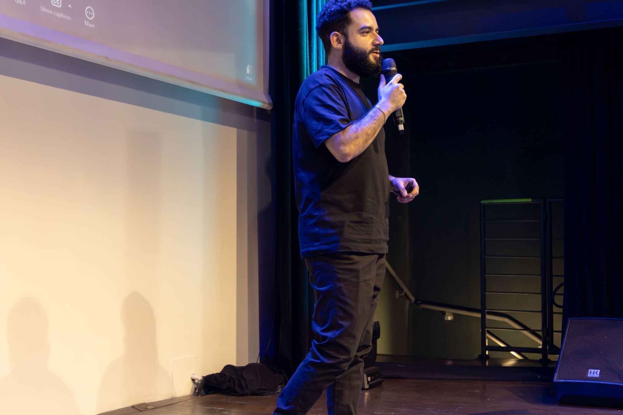 A speaker with a microphone on a conference stage in front of a projection screen