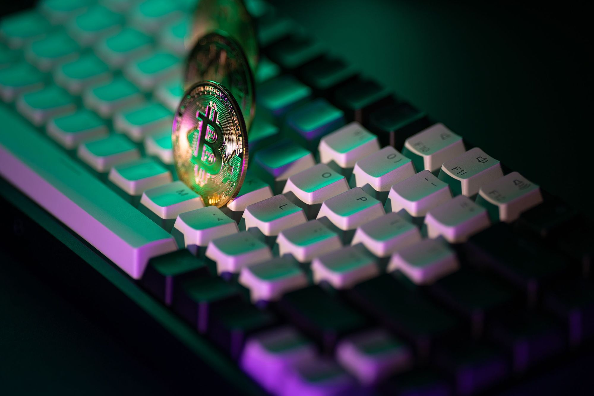 A Bitcoin coin lying on a keyboard lit in green and purple neon