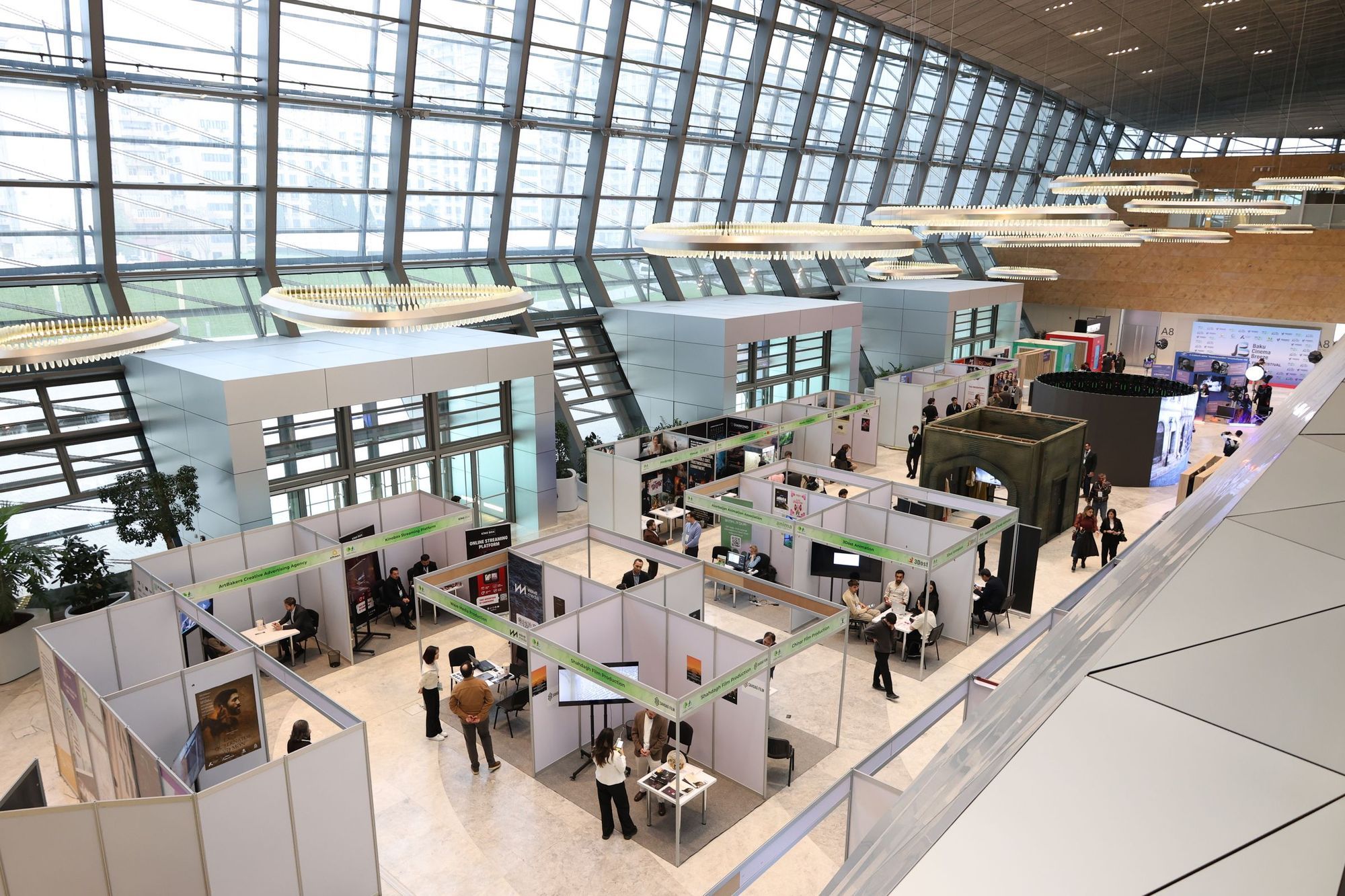 A large trade show hall with rows of exhibition booths under a glass roof