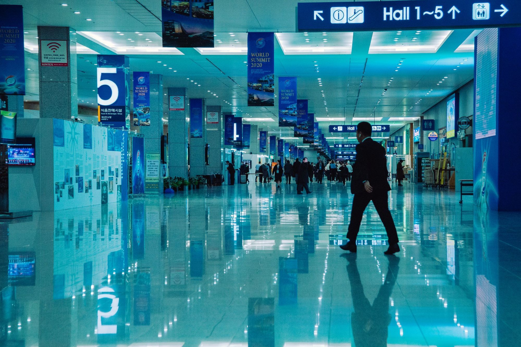 A bright conference venue corridor with hall signs and reflections on the floor