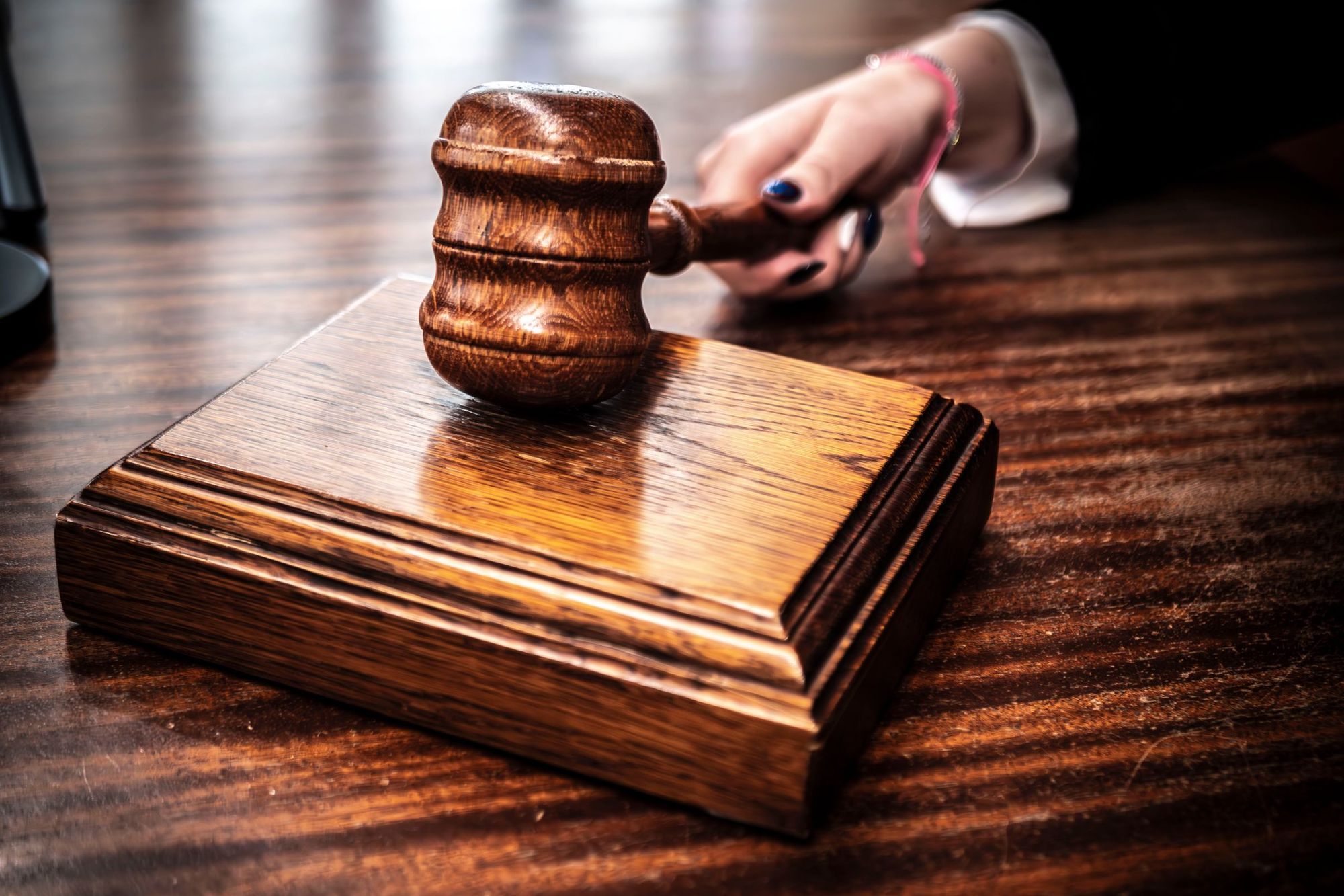 A hand resting a wooden judge's gavel on its sound block on a desk