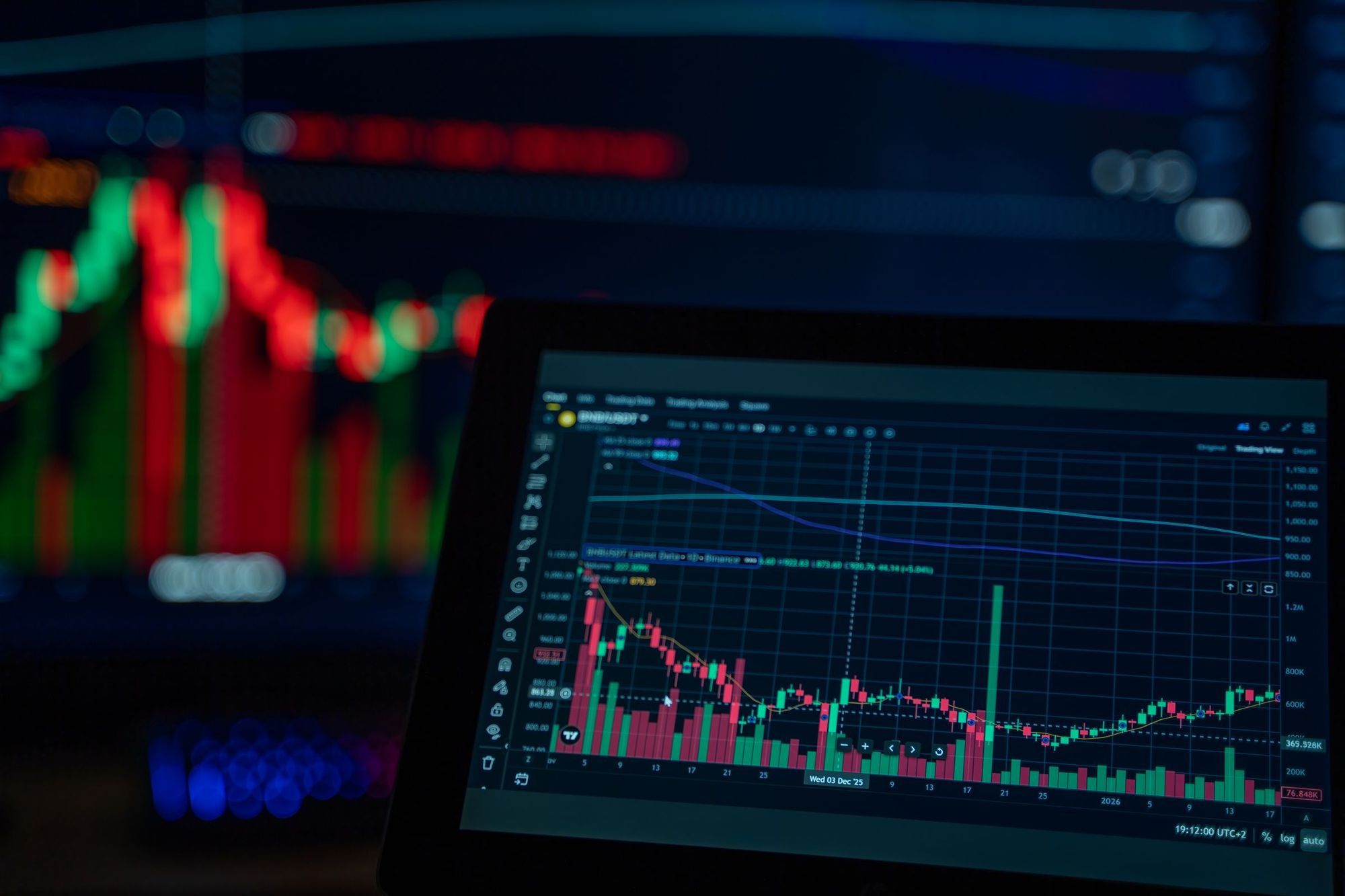 Market price charts glowing on a laptop and a monitor in a dark room